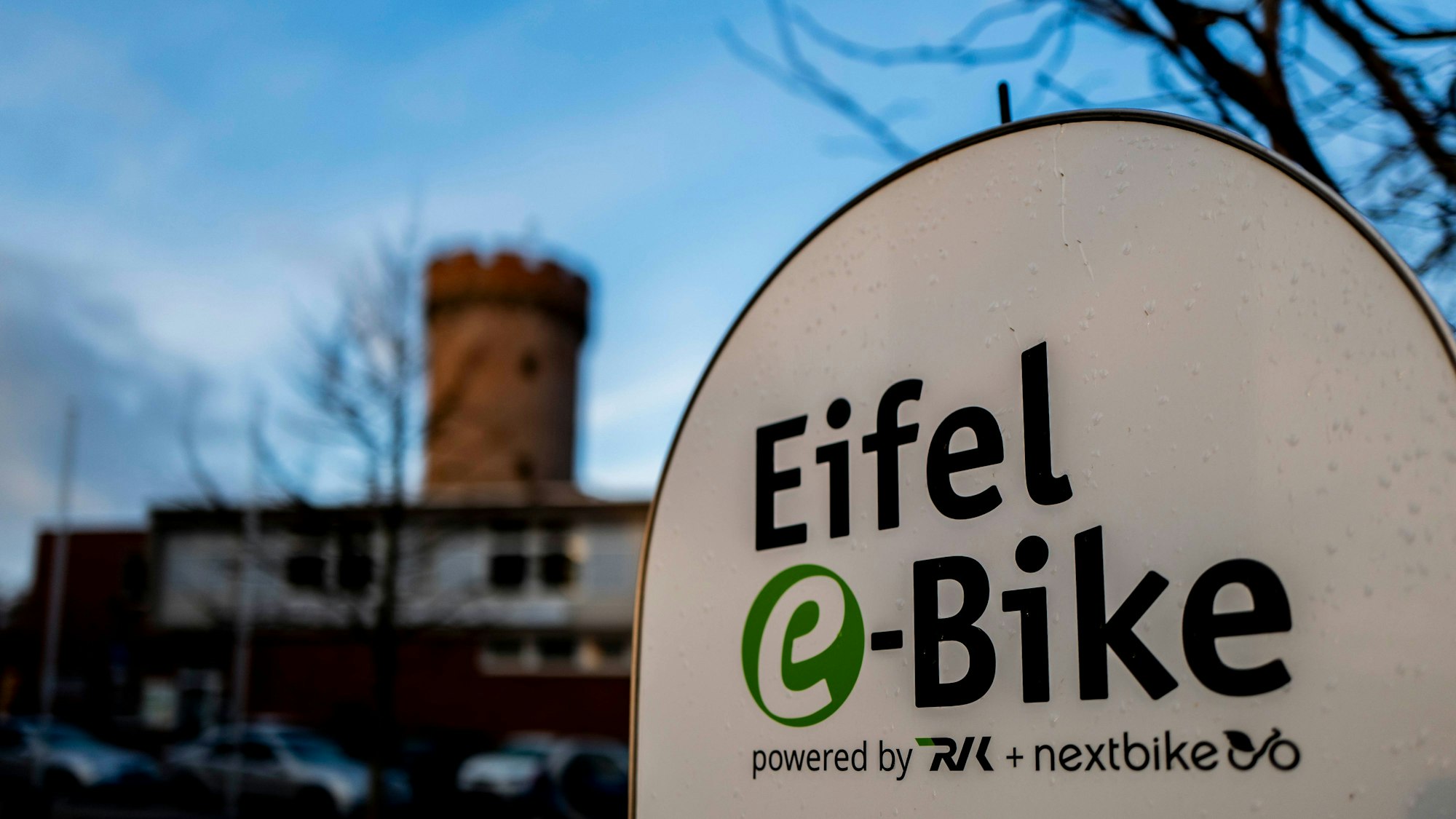 Das Bild zeigt im Vordergrund das Logo des Eifel-E-Bikes, im Hintergrund leicht unscharf die Zülpicher Landesburg.