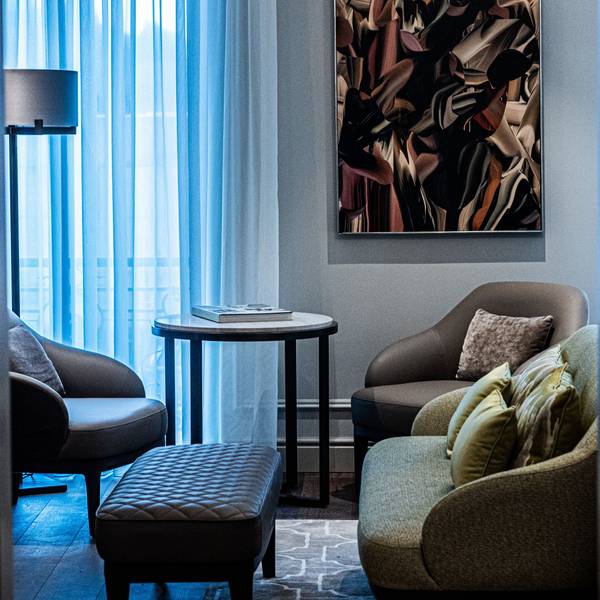 Der Blick durch die Tür der Suite zeigt ein kleines Sofa, vor der eine Lederbank steht. Im Hintergrund sind zwei Lederstühle mit einem Beistelltisch vor dem Fenster zu sehen.