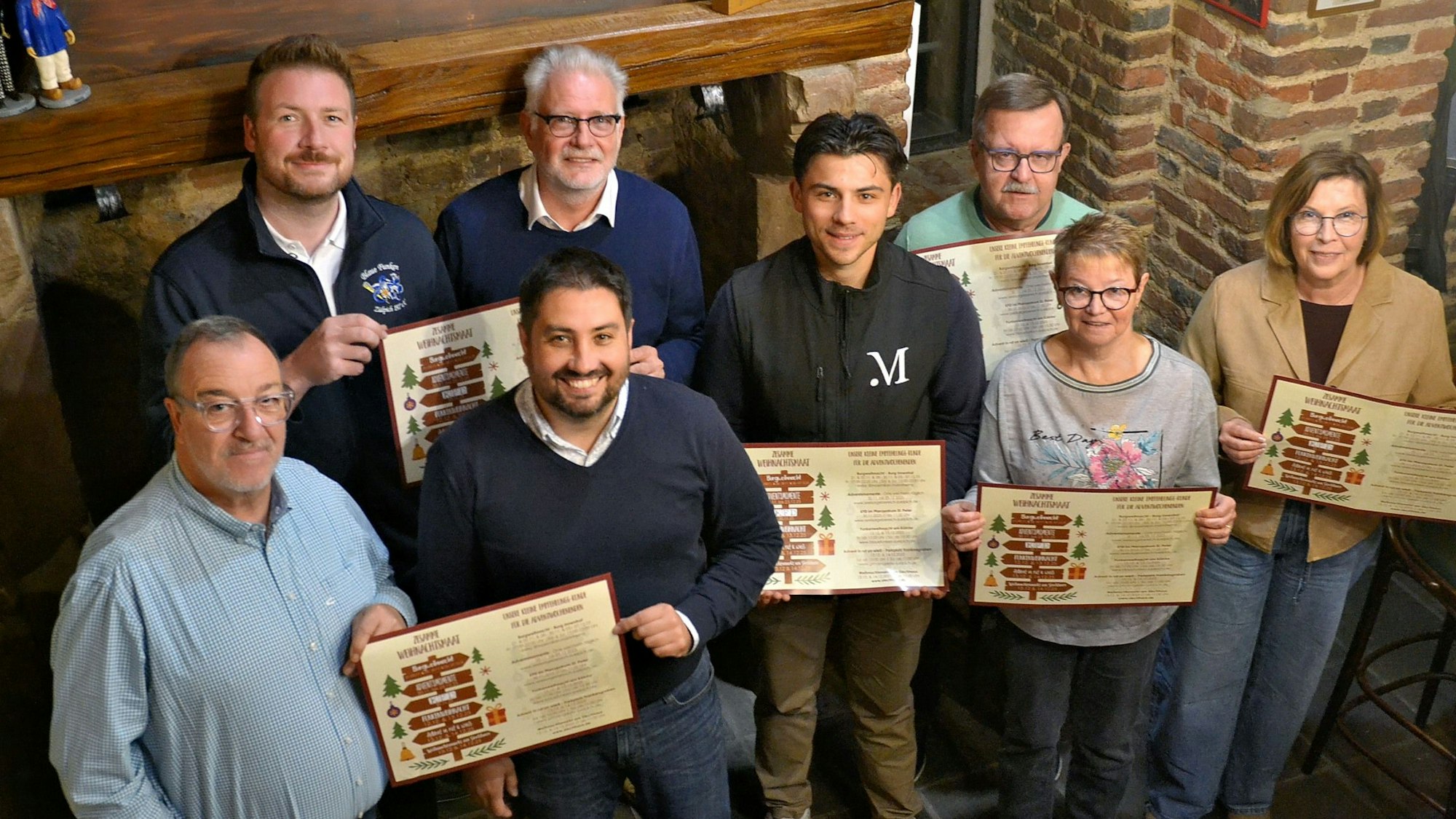 Acht Männer und Frauen haben sich zum Gruppenbild aufgestellt. Einige halten Tafeln mit dem Programm der Adventswochen.