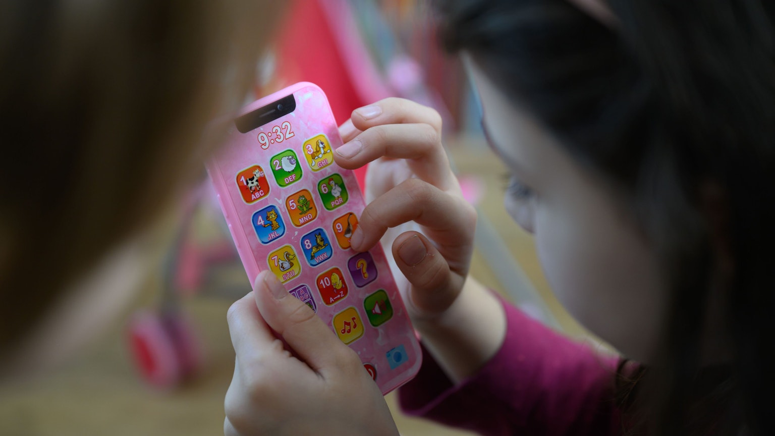 Ein Mädchen tippt auf einem rosa Spielzeughandy.