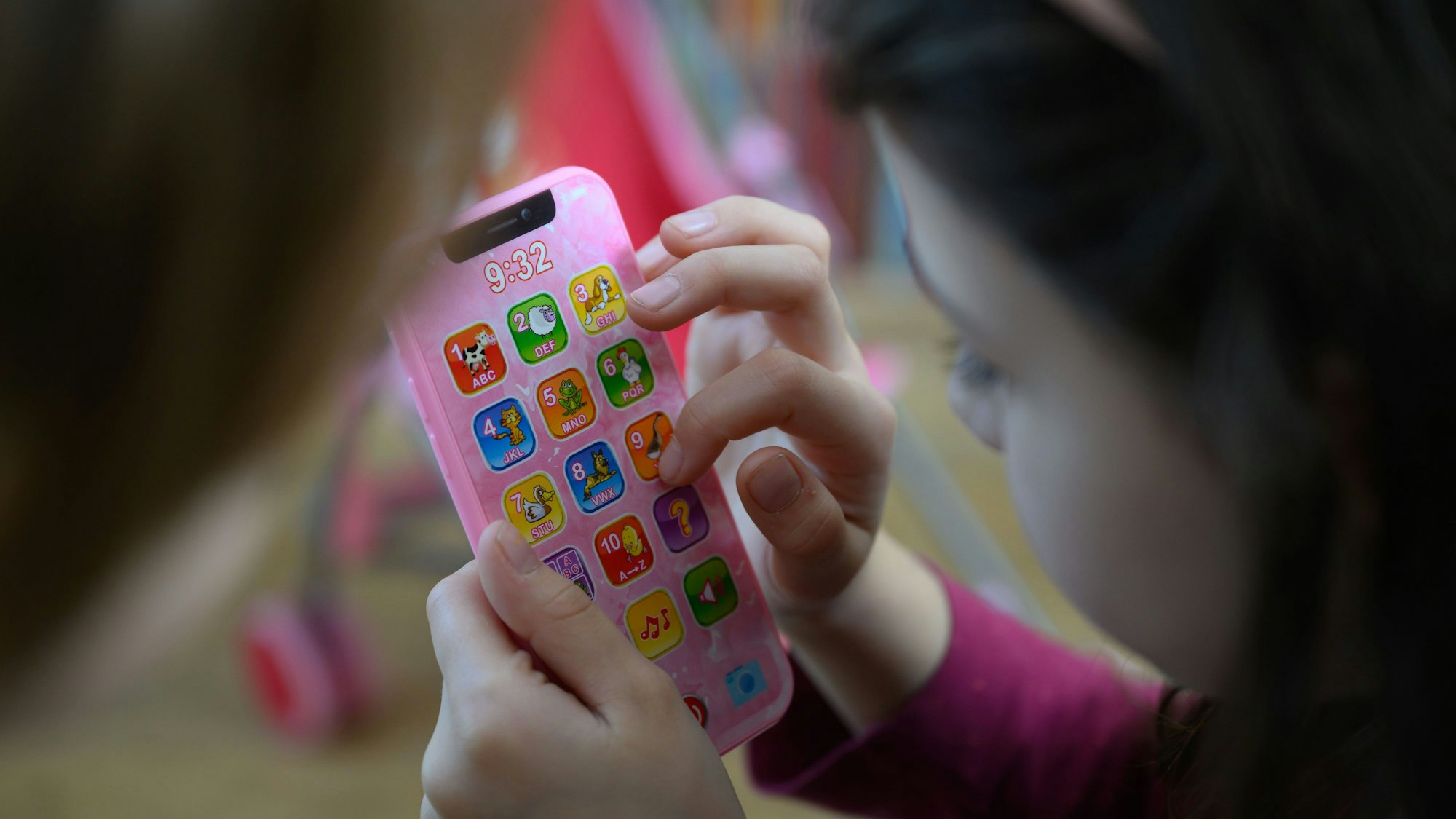 Ein Mädchen tippt auf einem rosa Spielzeughandy.