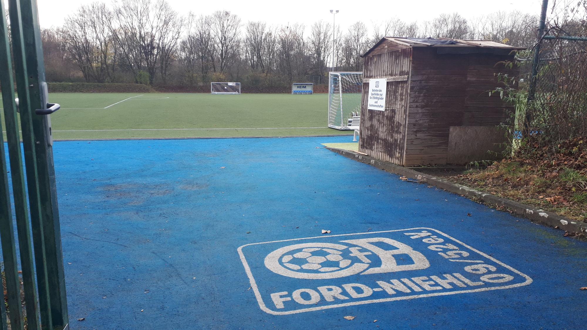 Ein blauer Bodenbelag hinter einem geöffneten Gittertor führt zu einem Trainingsgelände.