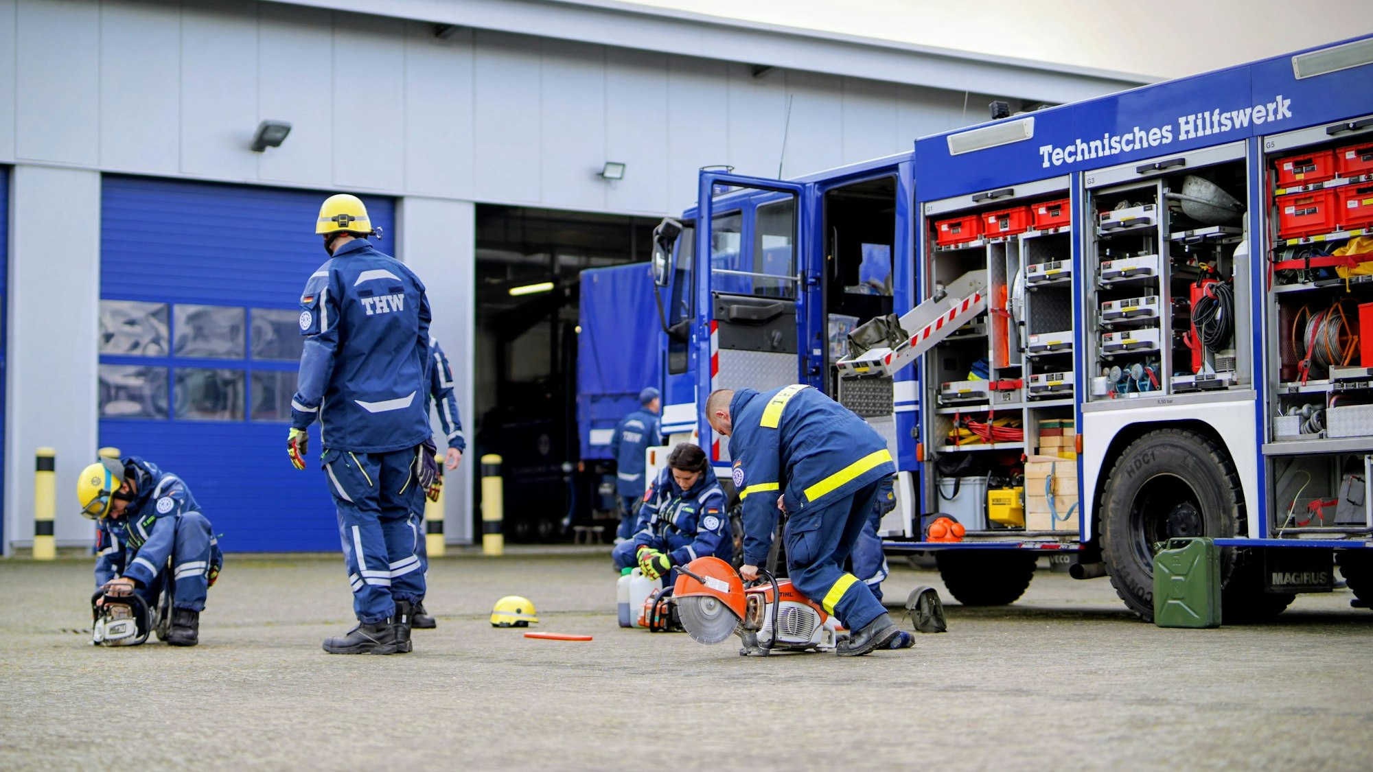 THW-Mitglieder kümmern sich um ihre Ausrüstung, im Hintergrund ist ihr Fahrzeug zu sehen.