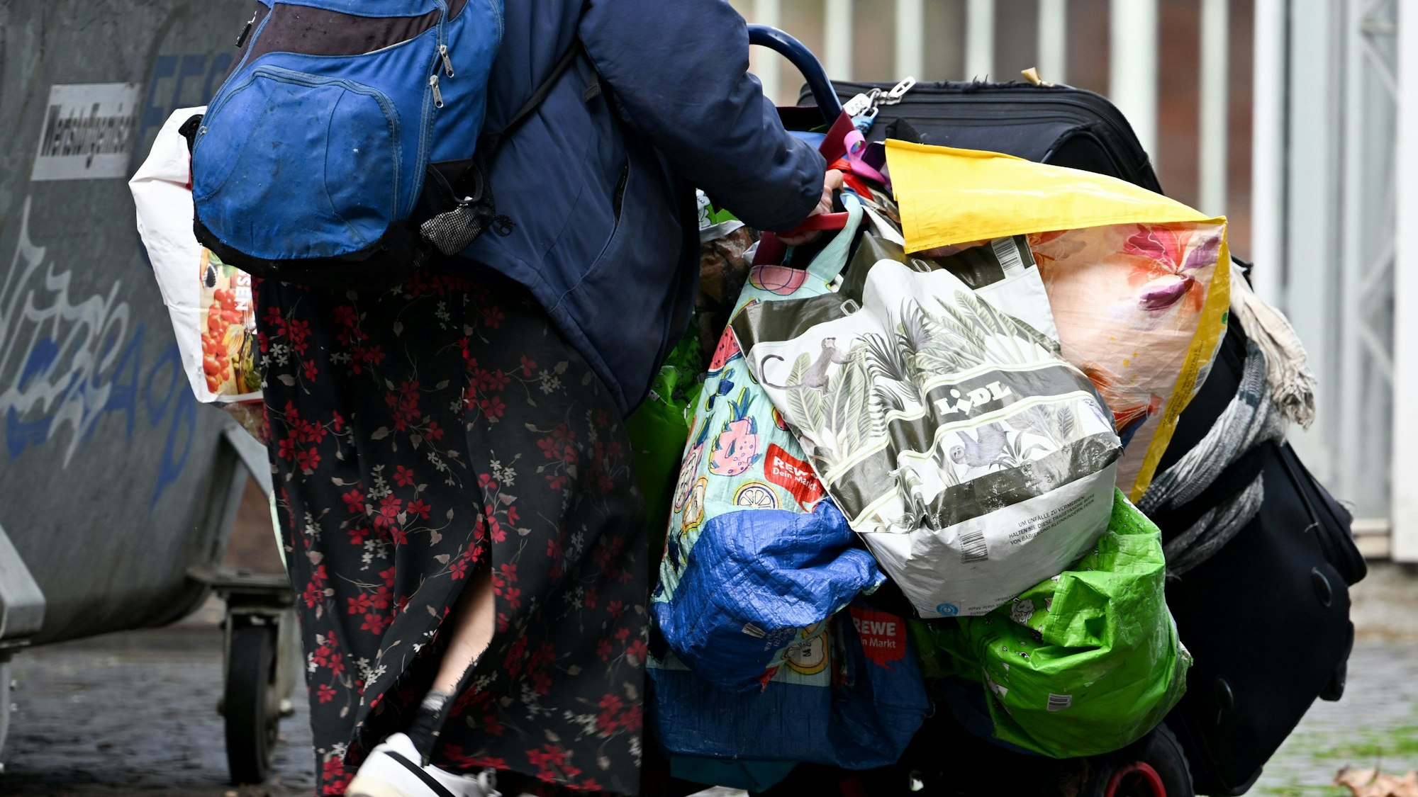 Eine obdachlose Frau schiebt ihr Hab und Gut mithilfe einer Transportkarre durch die Stadt.
