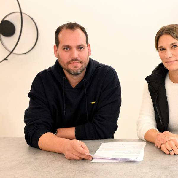 Ein Mann und eine Frau sitzen nebeneinander an einem Tisch mit Dokumenten vor sich liegen.