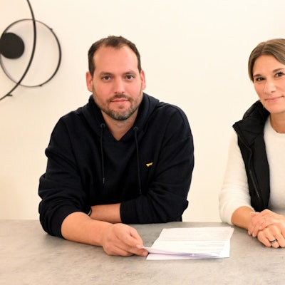 Ein Mann und eine Frau sitzen nebeneinander an einem Tisch mit Dokumenten vor sich liegen.