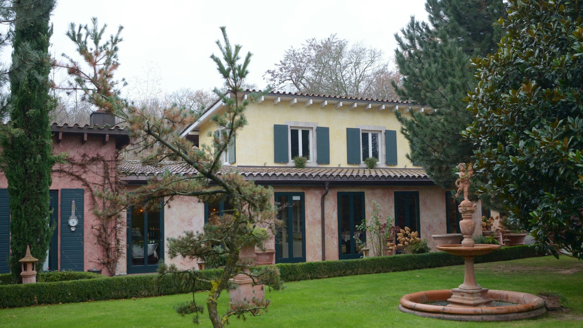 Vor dem Restaurant liegt eine gepflegte Rasenfläche mit Springbrunnen und Bäumen.