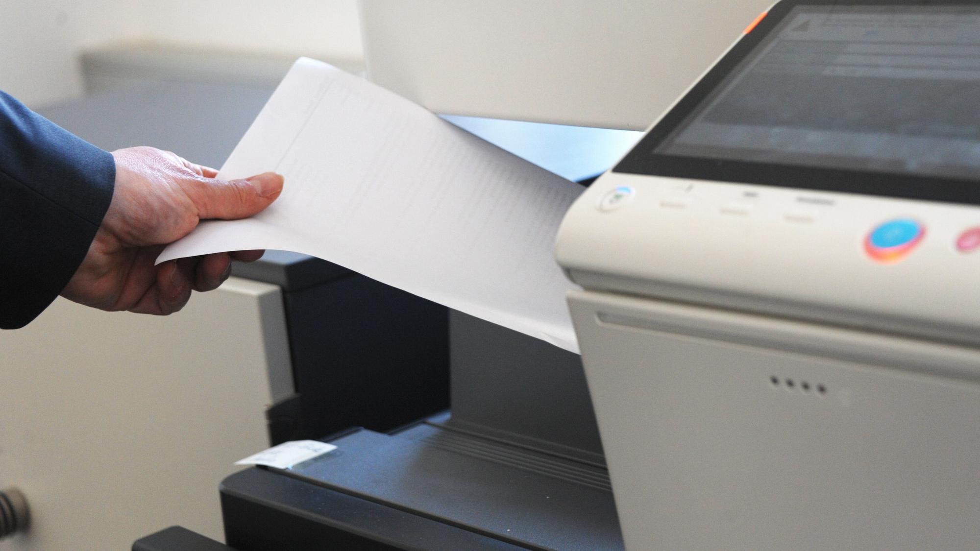 Eine Person holt Papier aus einem Kopierdrucker.