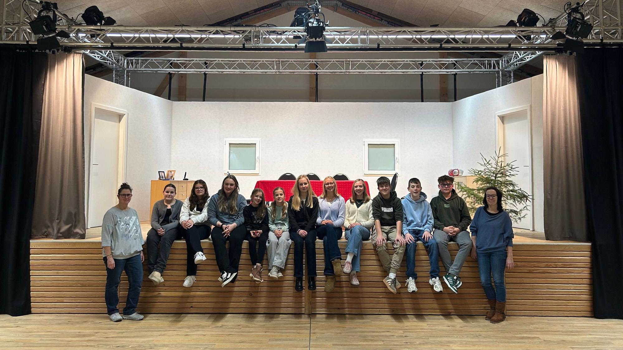 Die Mittglieder der Jugendgruppe des Theatervereins sitzen in einer Reihe am Bühnenrand.