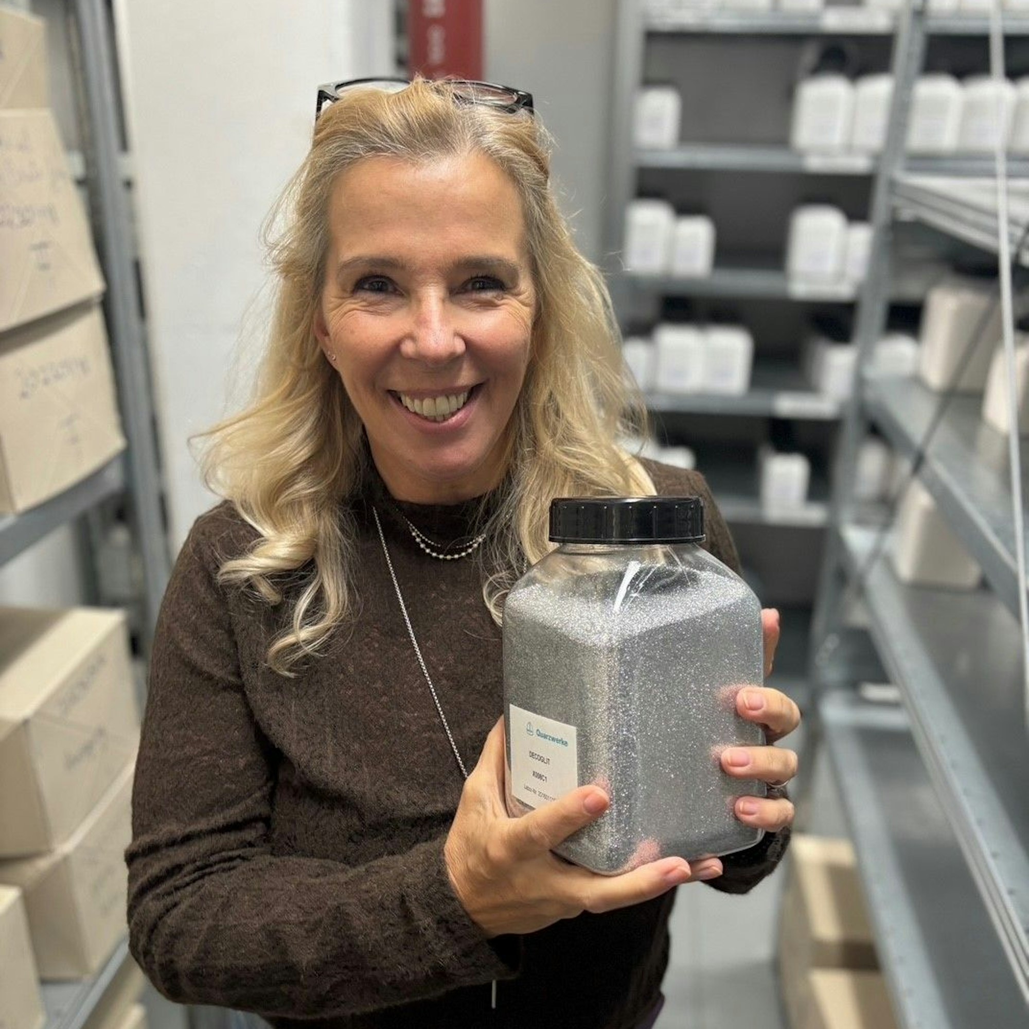 Auf dem Bild ist eine Frau in einem braunen Pullover zu sehen, die ein silbrig glänzende Produktprobe in den Händen hält.