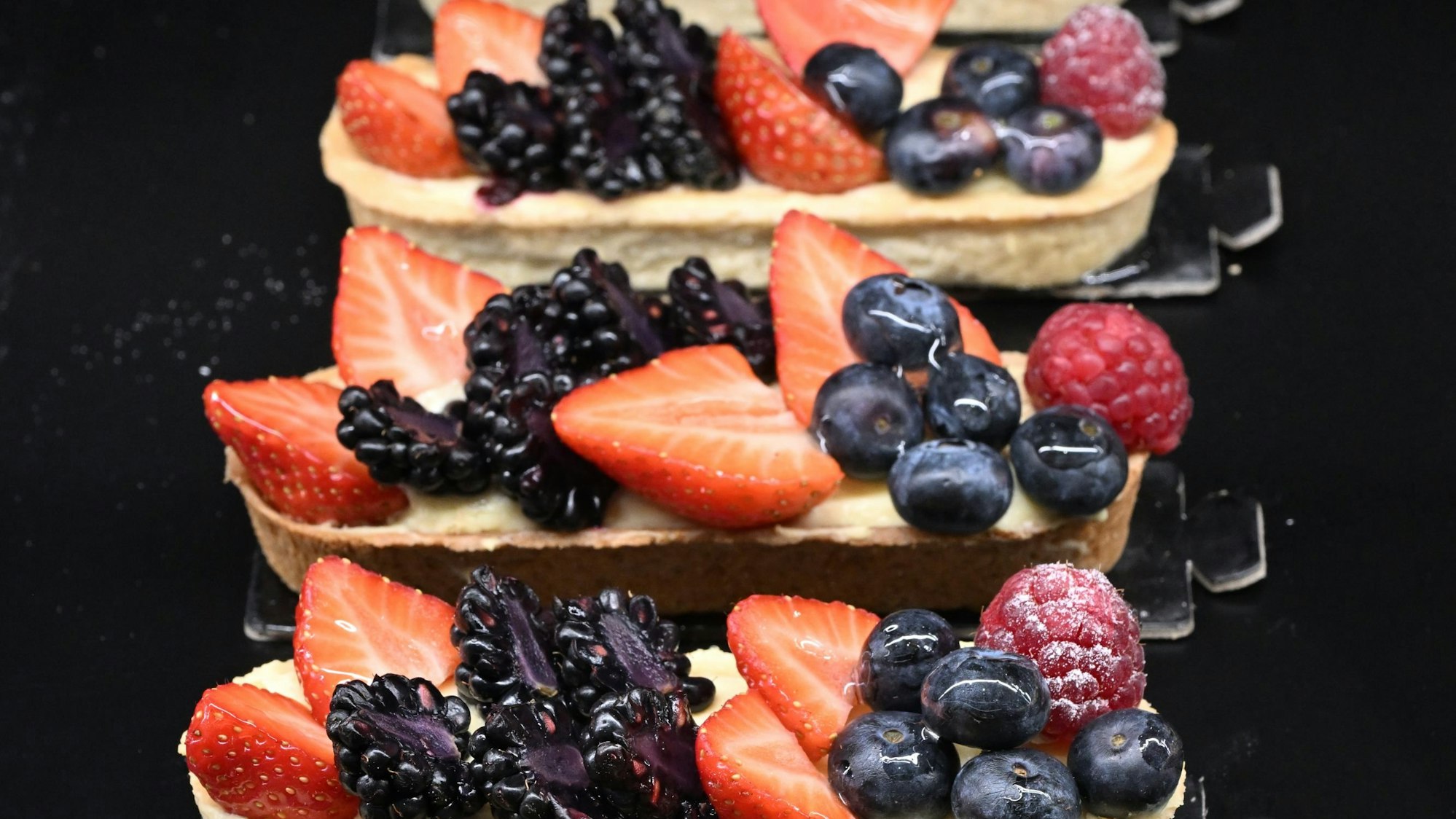 Gebäck mit Früchten liegen hintereinander auf einem Tablett.