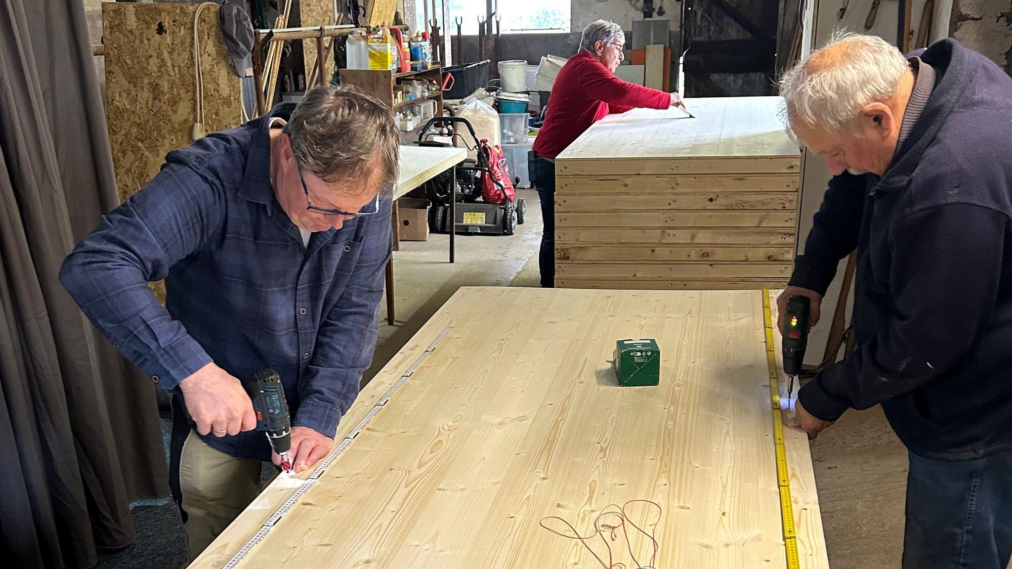 Drei Personen bauen in einer Werkstatt an den hölzernen Kulissenwänden.