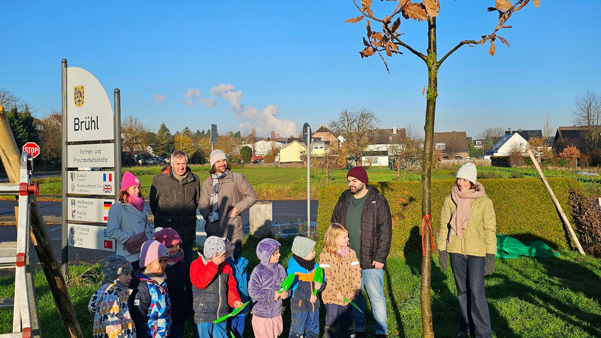 Kinder und Erwachsene stehen neben einem neu gepflanzten Baum.