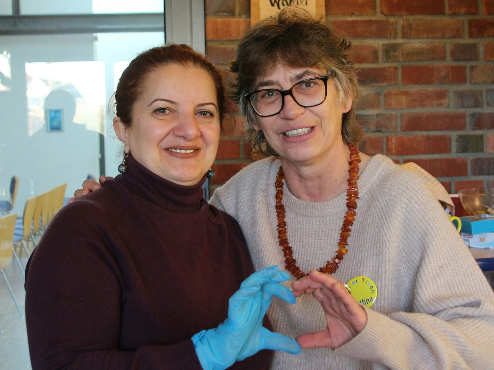 Das Foto zeigt zwei Frauen, die gemeinsam jeweils mit den Fingern einer Hand ein Herz bilden.