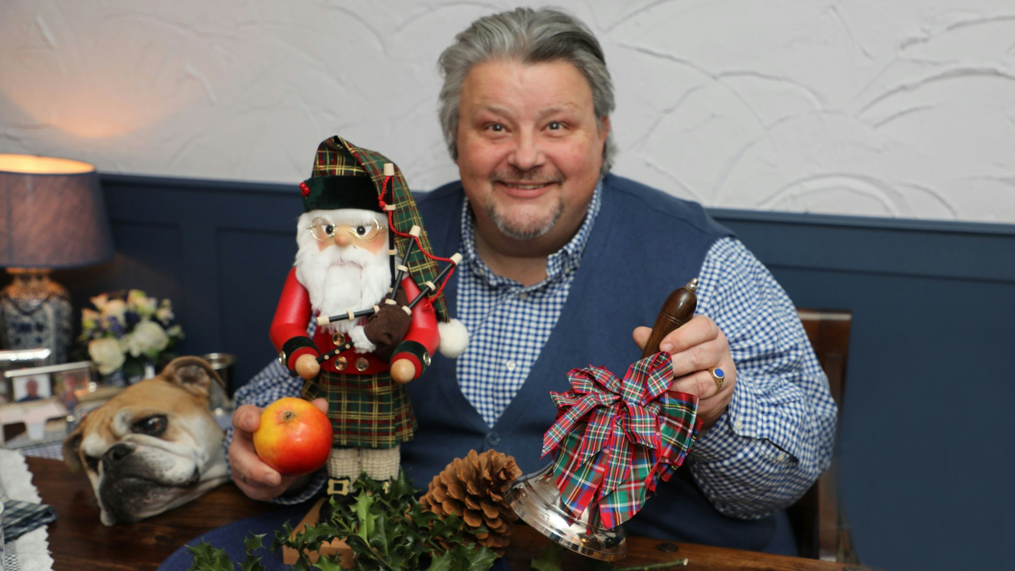 Ein Mann hat eine Glocke und einen Apfel in der Hand und lächelt.