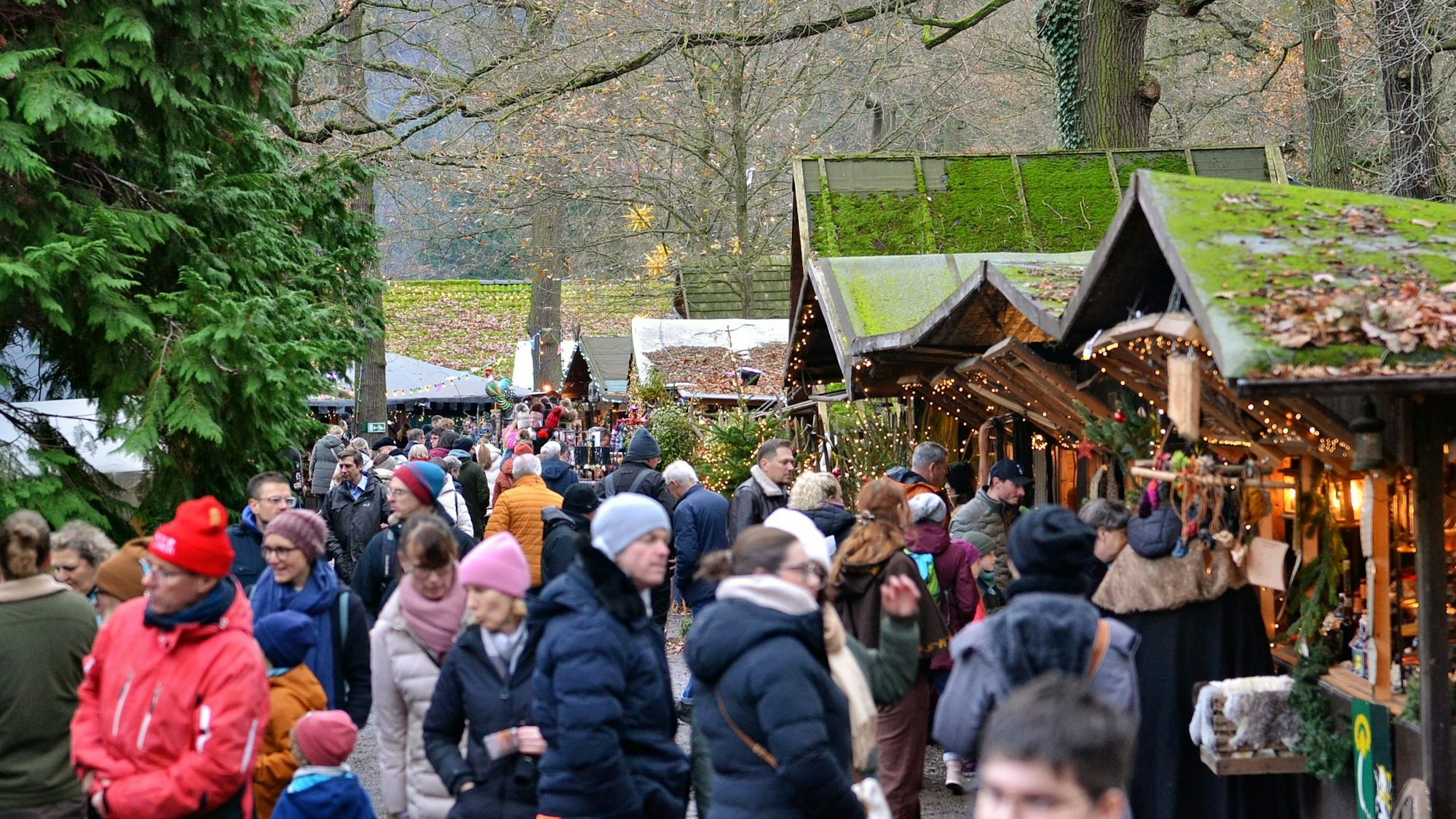Eine große Menge Besucher laufen entlang der Buden, deren Dächer mit Moss bewachsen sind.