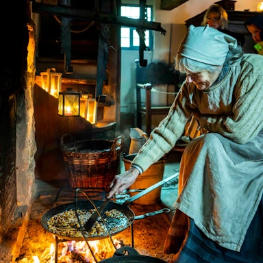 Das Bild zeigt Andrea Rolfes-Koenen in einem historischen Outfit, während sie in einer Pfanne Mandeln zubereitet.