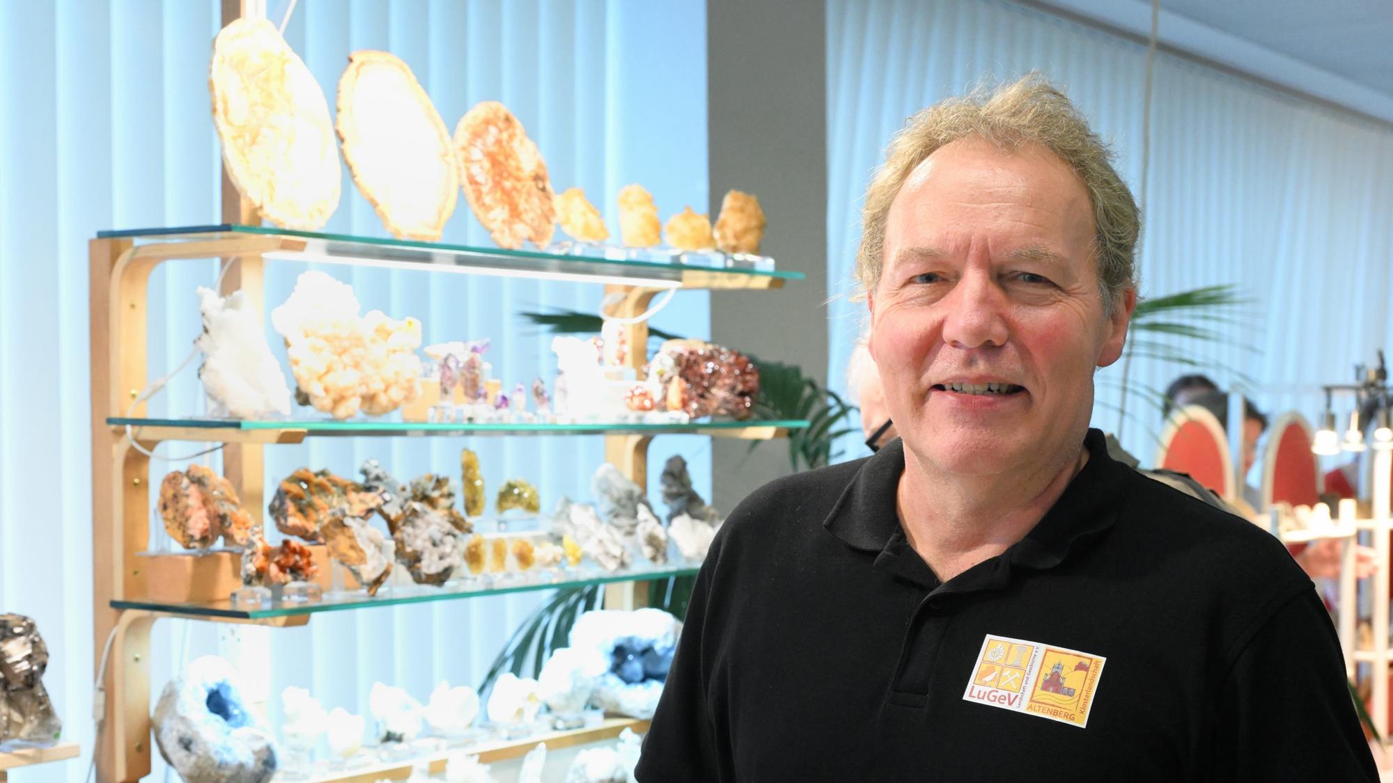 Diplom-Geologe Randolf Link steht vor einem Regal mit bunten Mineralien.
