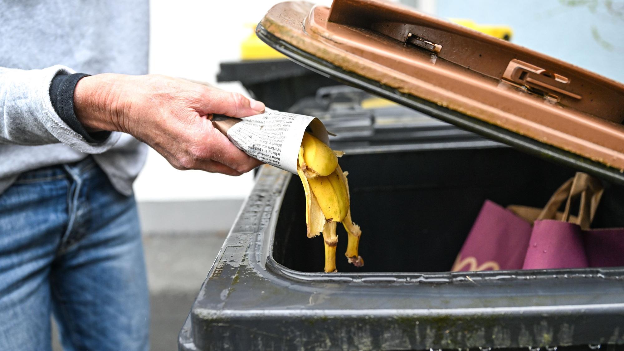 Jemand wirft eine leere Bananenschale in eine Biotonne.