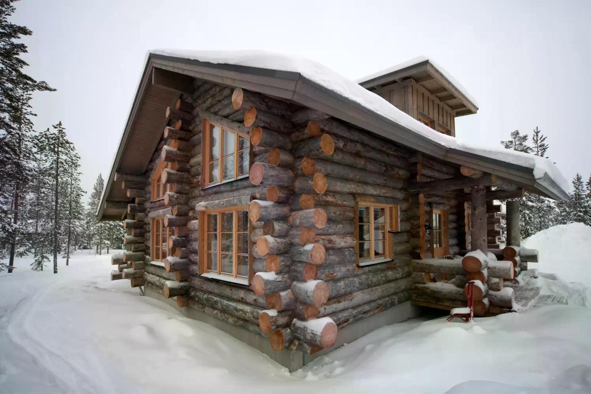 Das Bild zeigt eine gemütliche Hütte im verschneiten Winterwald in Finnisch-Lappland