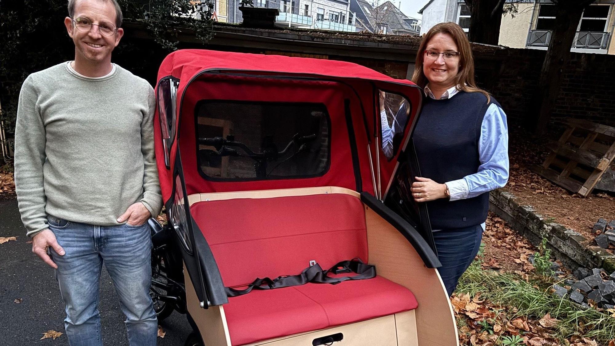 Auf dem Bild sind eine Frau und ein Mann neben einer Rikscha zu sehen.