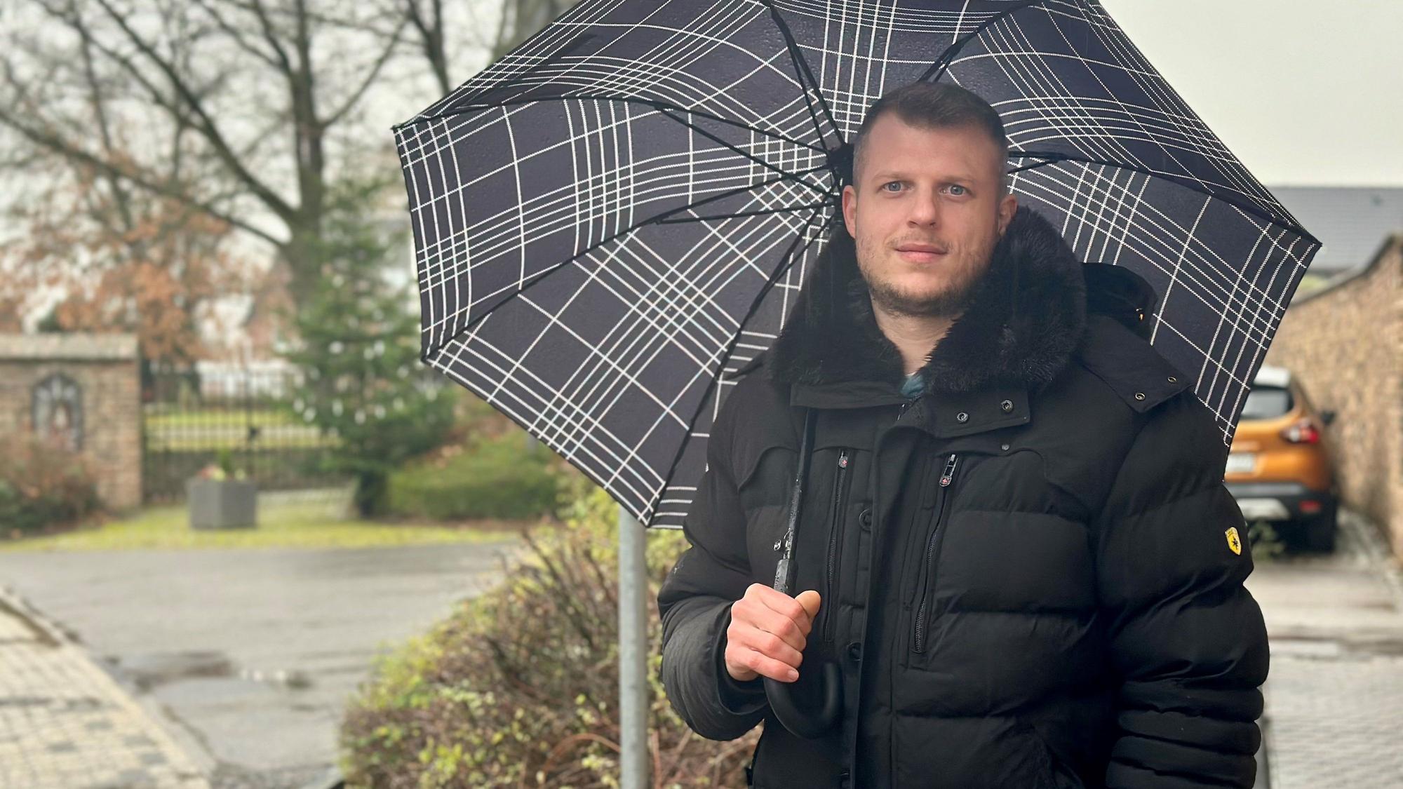 Ein Mann mit Schirm steht an einer Straße.