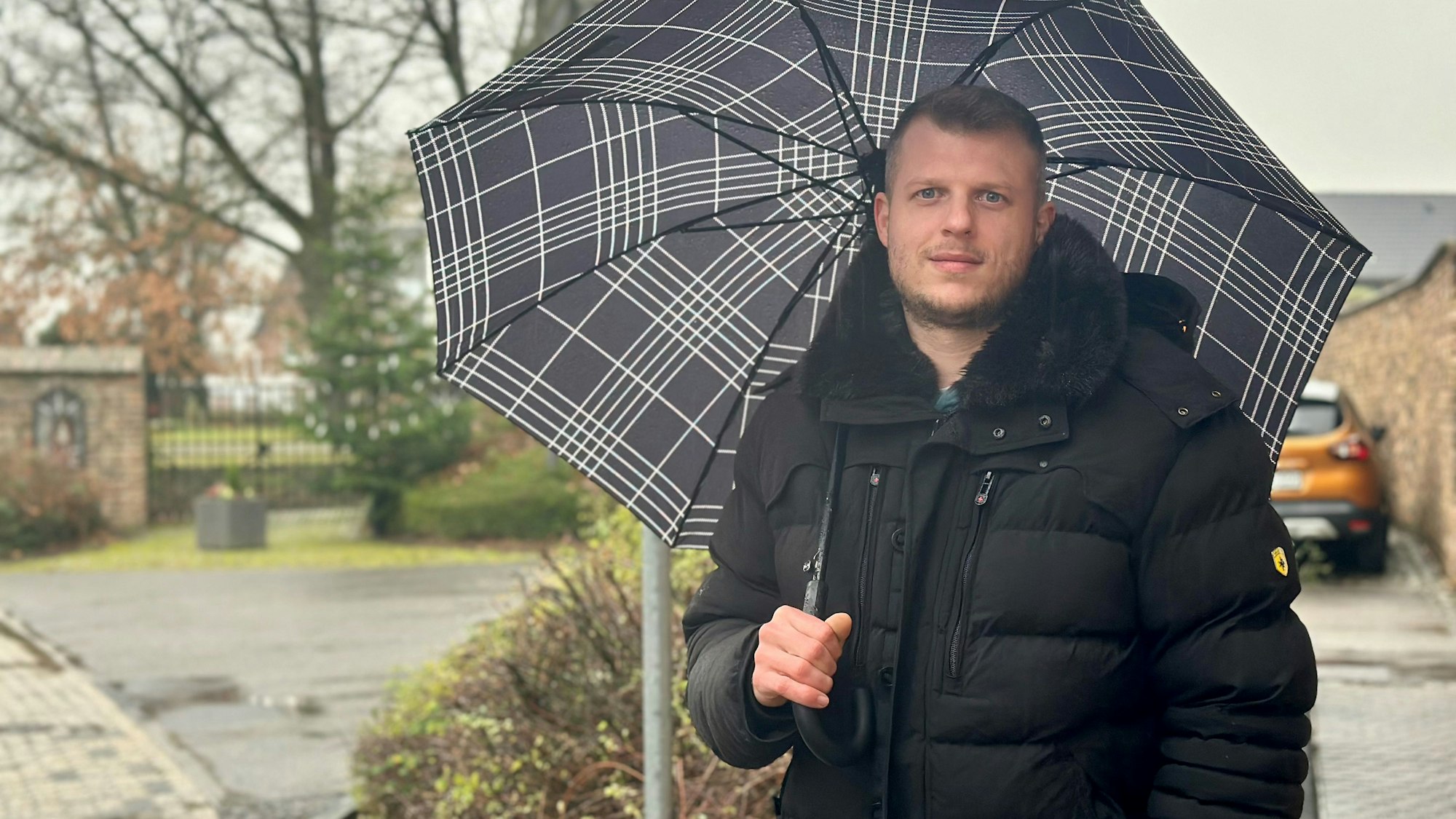 Ein Mann mit Schirm steht an einer Straße.