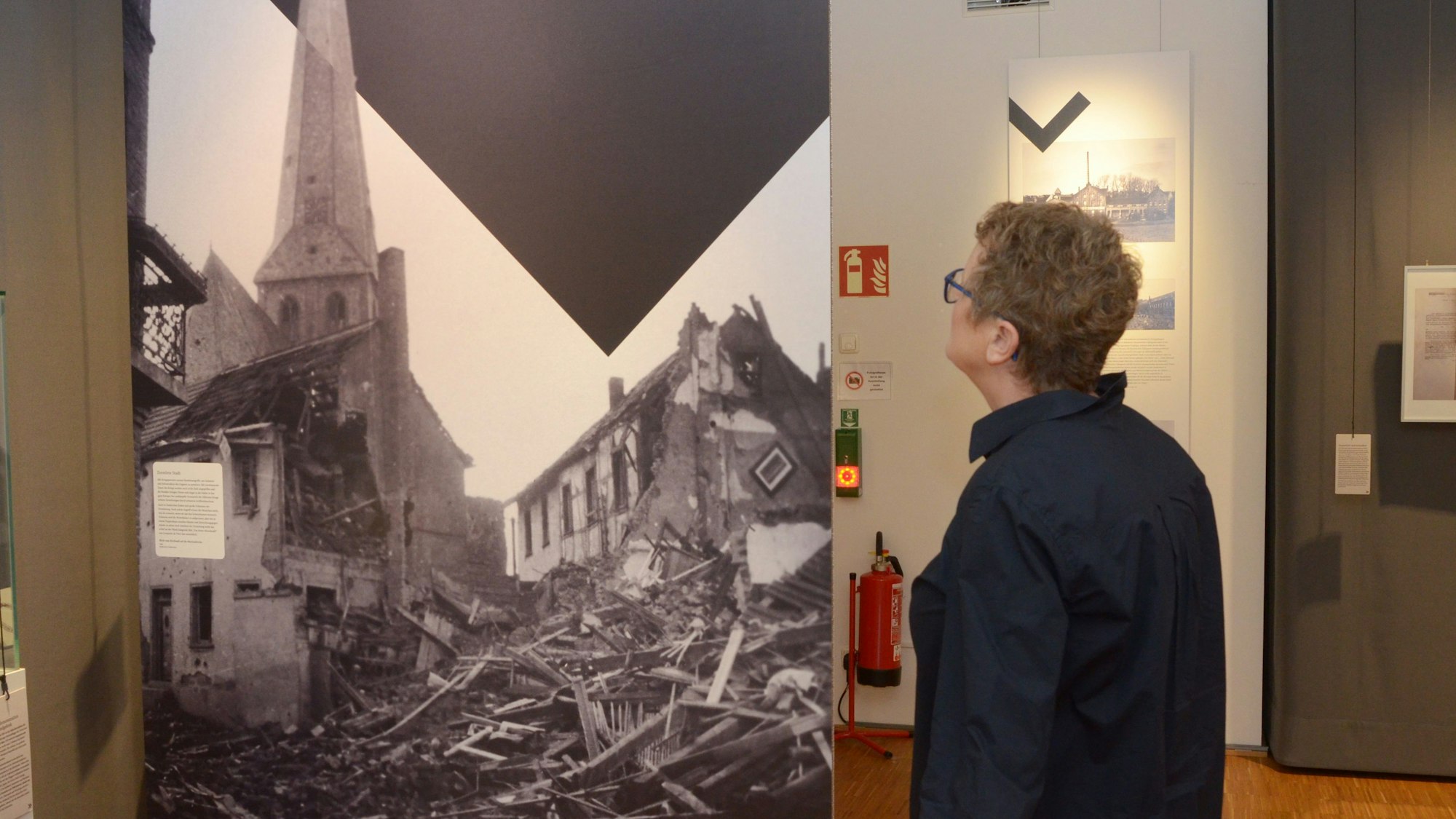Eine Frau betrachtet ein großformatiges Foto, das die Zerstörung von Häusern in Euskirchen während des Zweiten Weltkrieges zeigt.