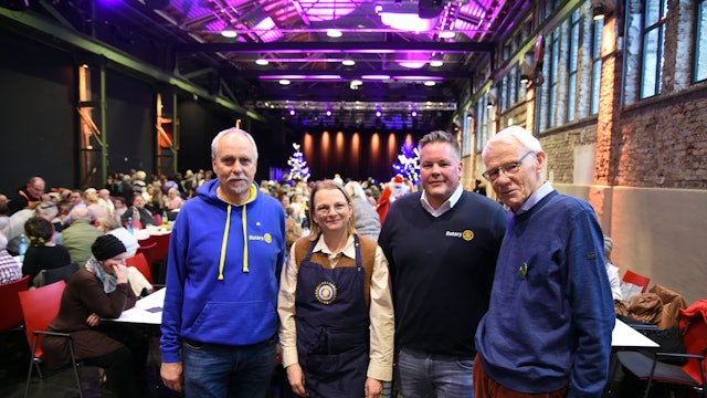 Vier Personen in einem Saal mit langen Tischen.