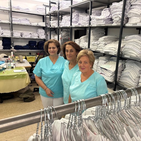 Auf dem Foto sind drei Frauen in Arbeitskleidung und viele weiße Wäschestücke zu sehen.