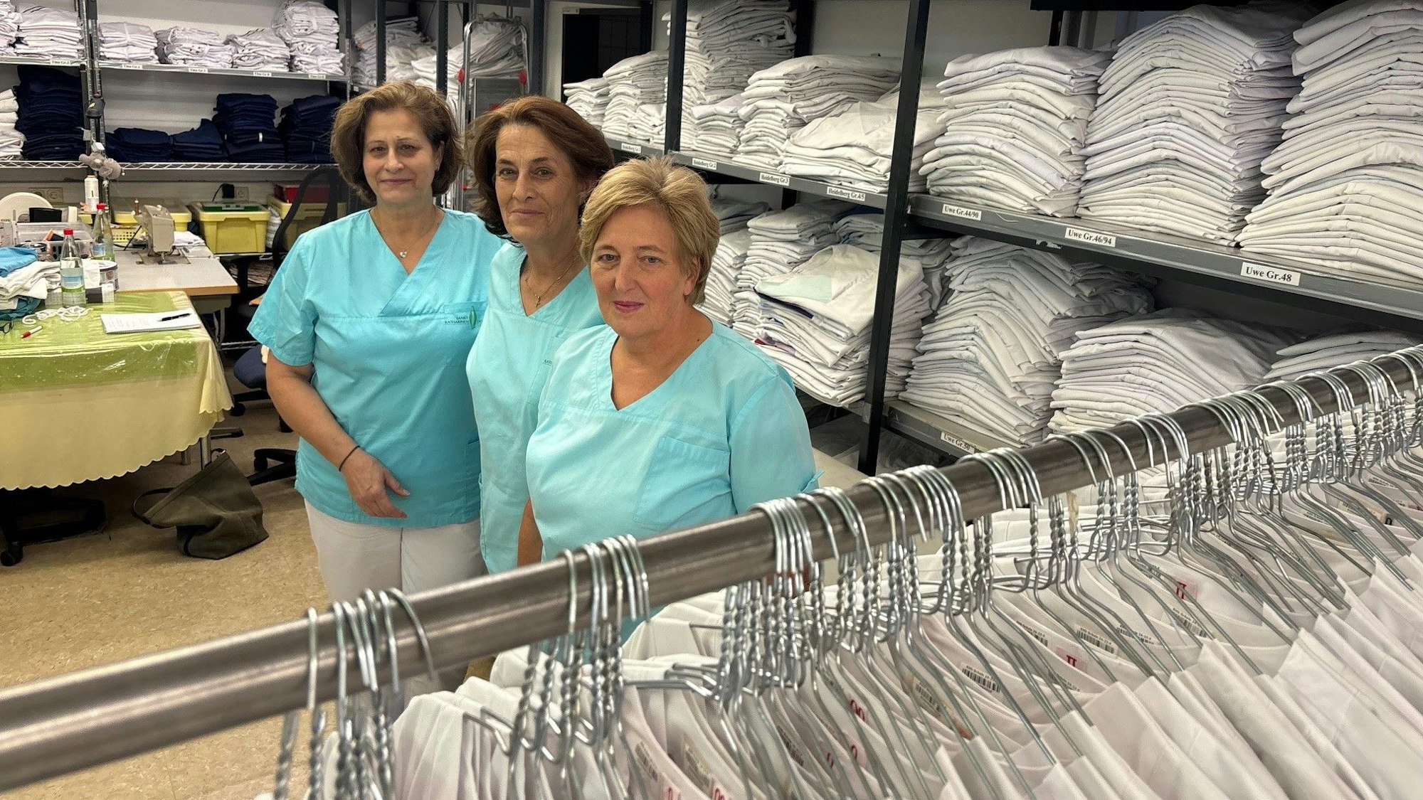 Auf dem Foto sind drei Frauen in Arbeitskleidung und viele weiße Wäschestücke zu sehen.