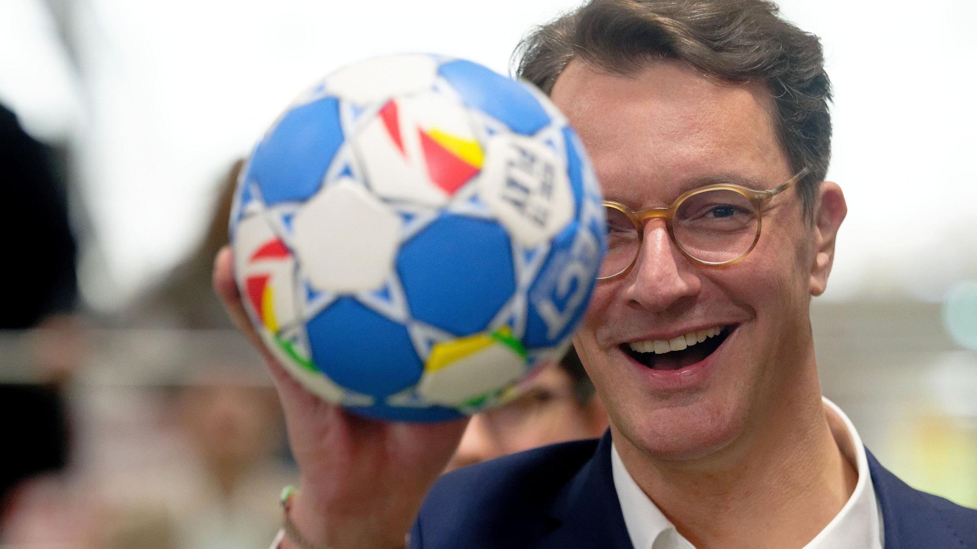 Hendrik Wüst (CDU), Ministerpräsident von Nordrhein-Westfalen deutet bei einer Pressekonferenz über Neuerungen des Bewerbungskonzepts für die olympischen und paralympischen Spiele einen Wurf mit einem Handball an.