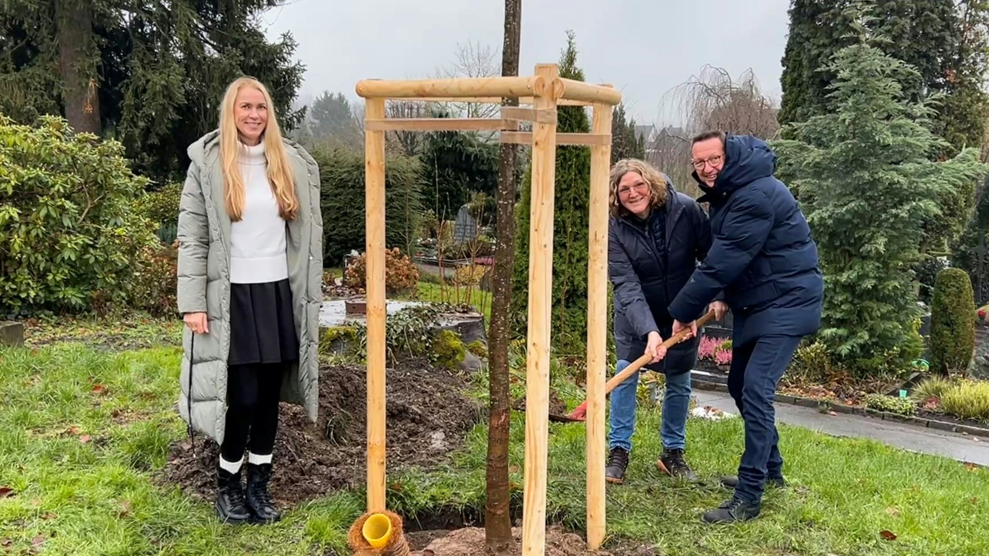 Umweltbeauftragte Svenja Mühlsiegl, Spenderin Ute Hentschel von den Grünen und Bürgermeister Dirk Runge pflanzen Winterlinden auf dem Friedhof Altenberger Straße.
