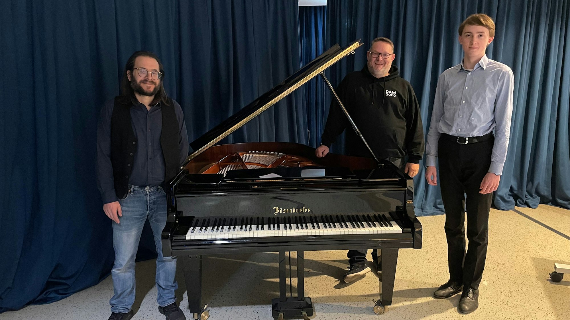 Zwei Männer und ein Schüler stehen um einen Flügel herum.