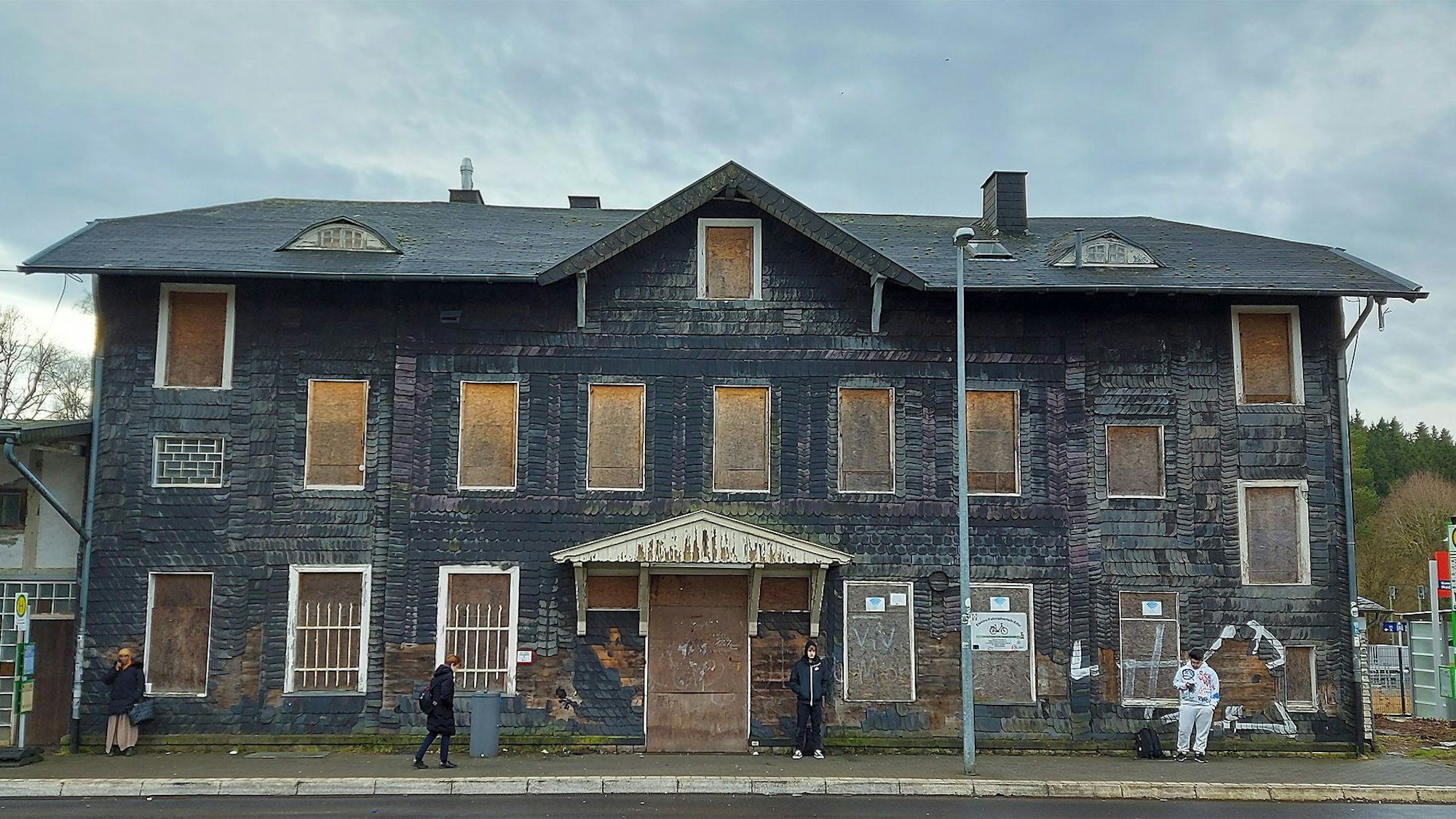 Das Bild zeigt das ehemalige Bahnhofsgebäude. Die Fenster und Türen sind mit Holzplatten zugenagelt.