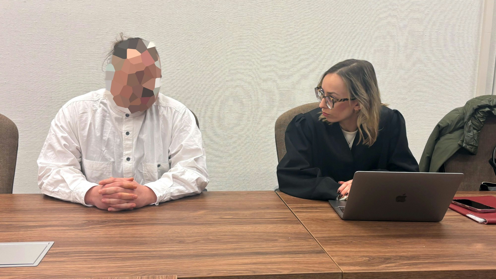 Ein Mann in einem weißen Hemd und mit verpixeltem Gesicht sitzt neben einer Frau in einer Anwaltsrobe.