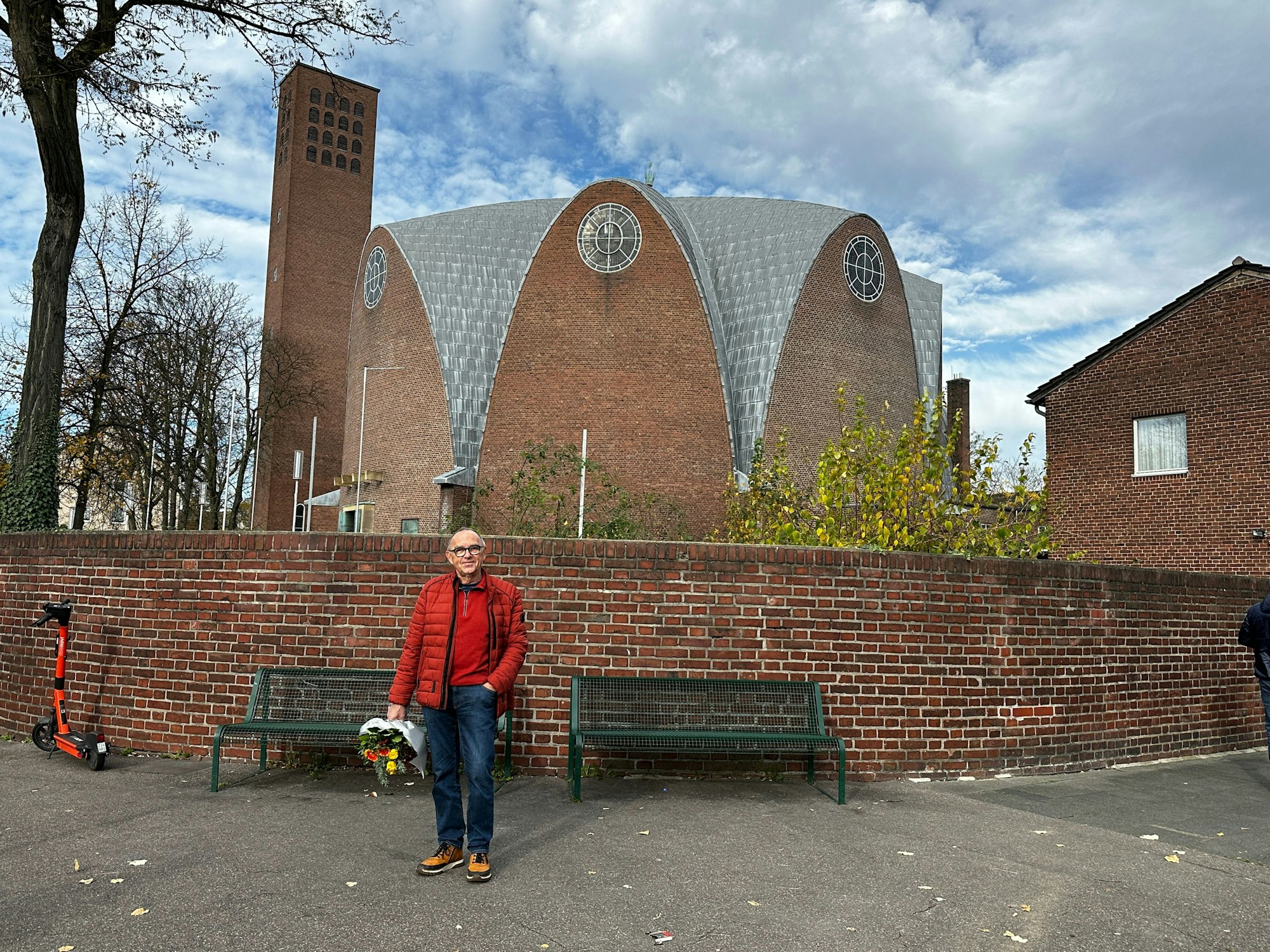 Ein Mann in Jeans und roter Jacke steht vor einer Kirche.