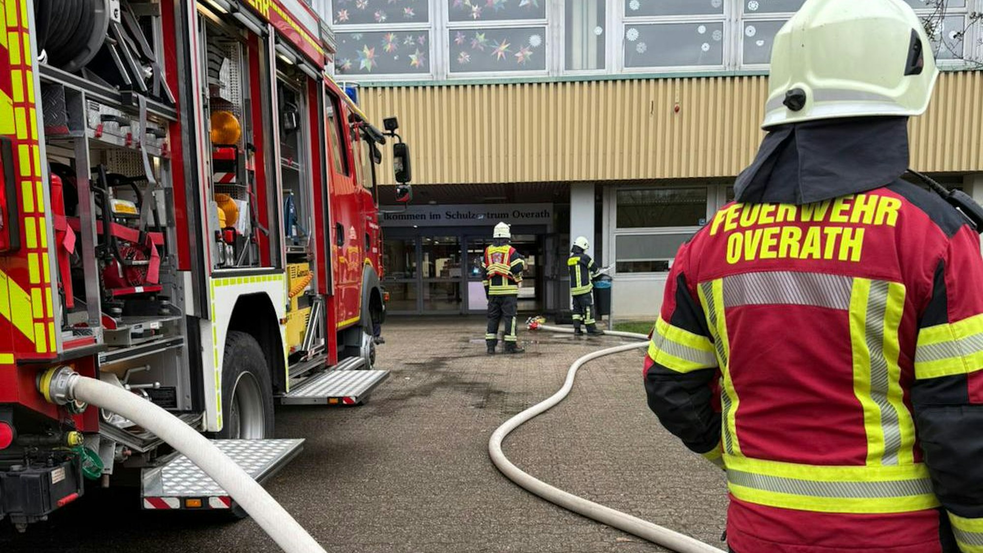 Feuerwehrleute stehen mit einem Löschfahrzeug vor dem Overather Schulzentrum Cyriax.