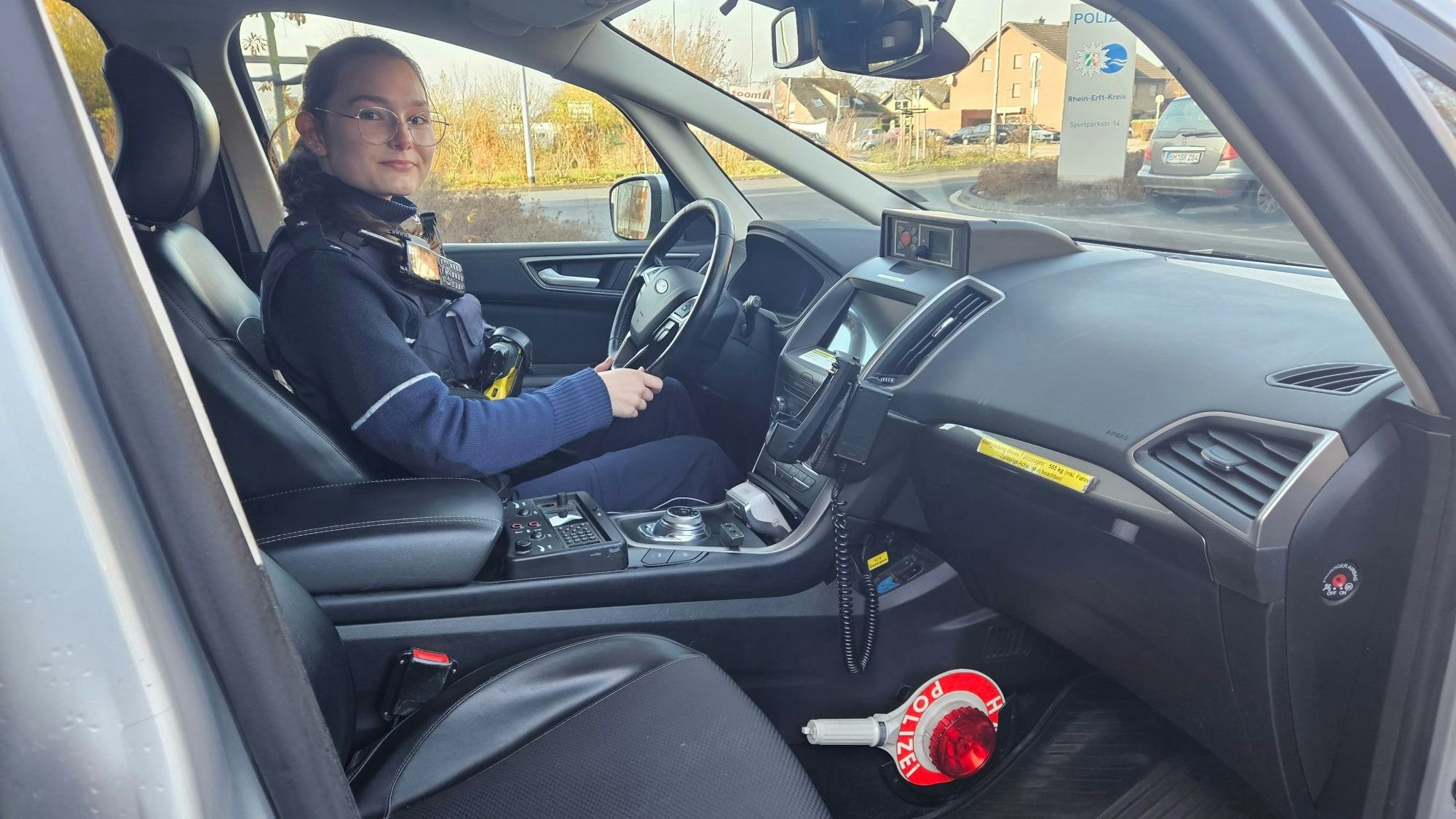 Zu sehen ist eine Polizistin am Steuer eines Streifenwagens.