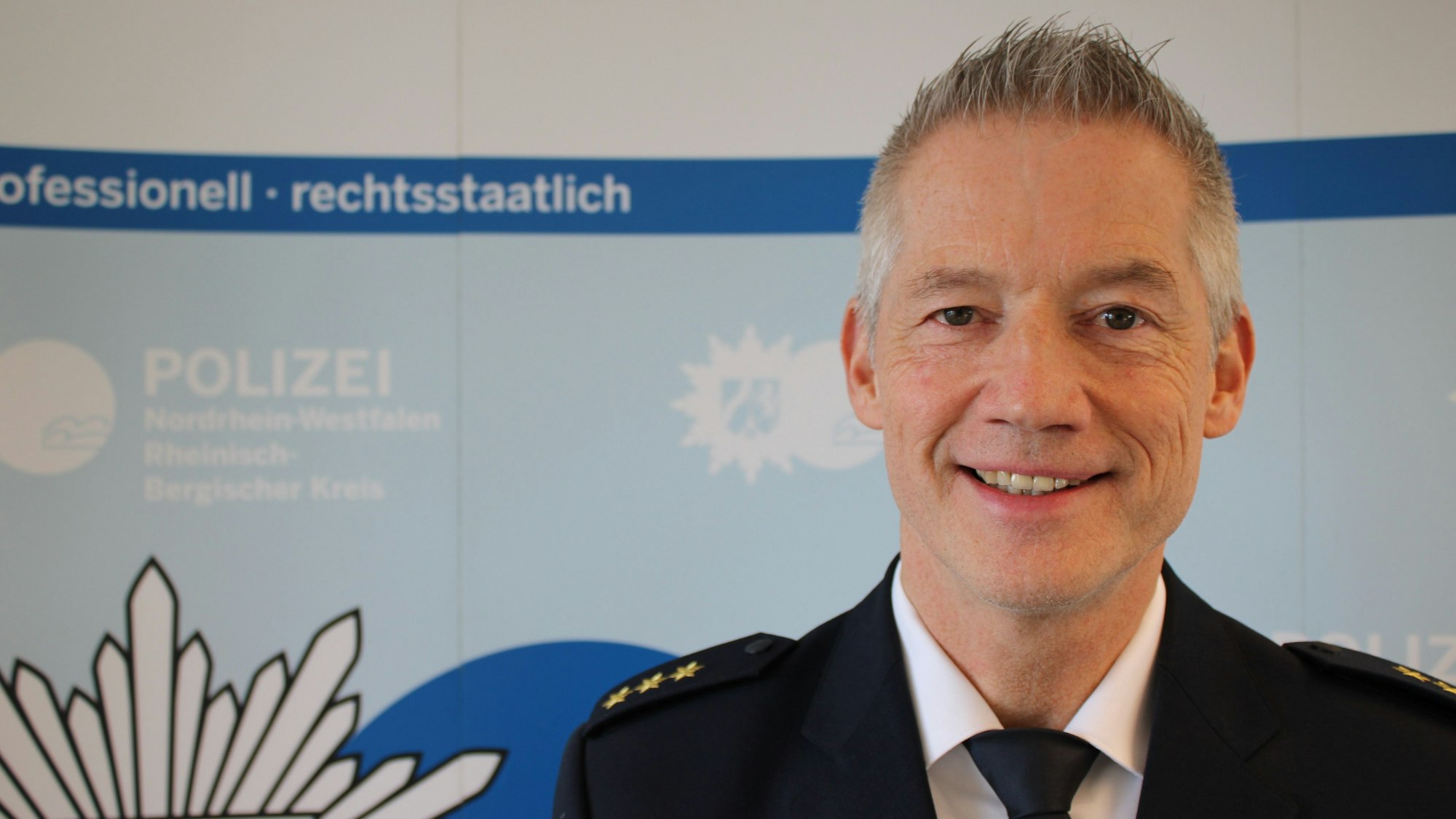 Polizeidirektor Achim Cüppers steht vor einer Werbewand der Polizei Rhein-Berg.