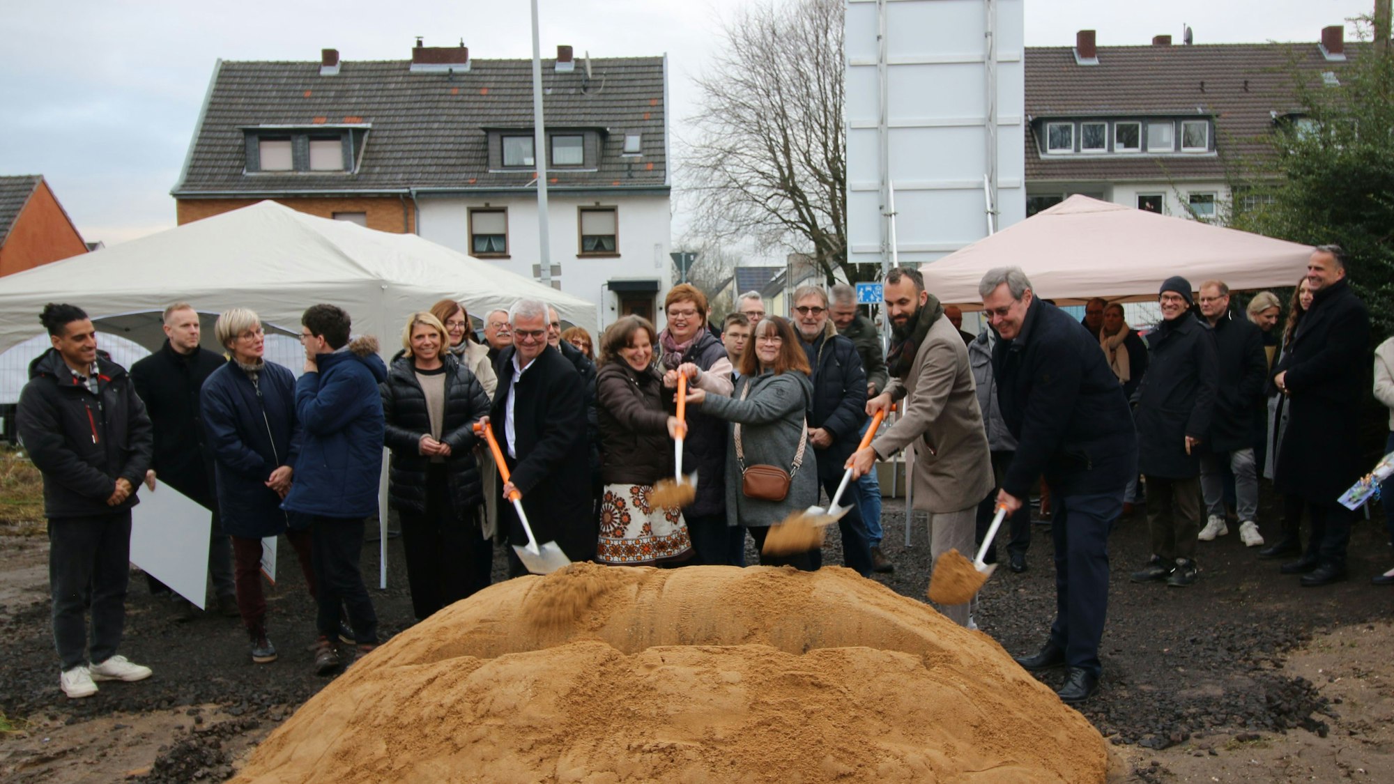 Zu sehen sind Menschen, die zum Spaten greifen, um den symbolischen Spatenstich auszuführen.