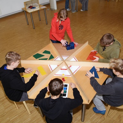 Kinder sitzen an einem Tisch im Kreis und knobeln.