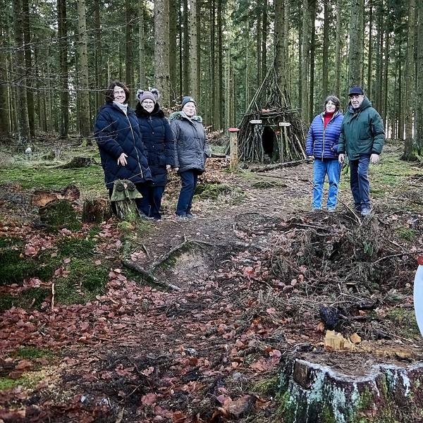 Mitten im Wald stehen die Personen, die den Krippenweg vorgestellt haben. Im Hintergrund sieht man die Schutzhütte, im Vordergrund einen selbstgebastelten Papp-Schneemann mit Schal.
