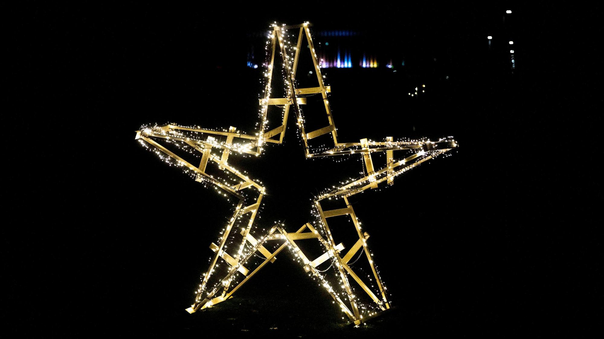 Das Bild zeigt einen aus Holzböcken zusammengebauten Holzstern samt leuchtender Lichterkette in der Dunkelheit.