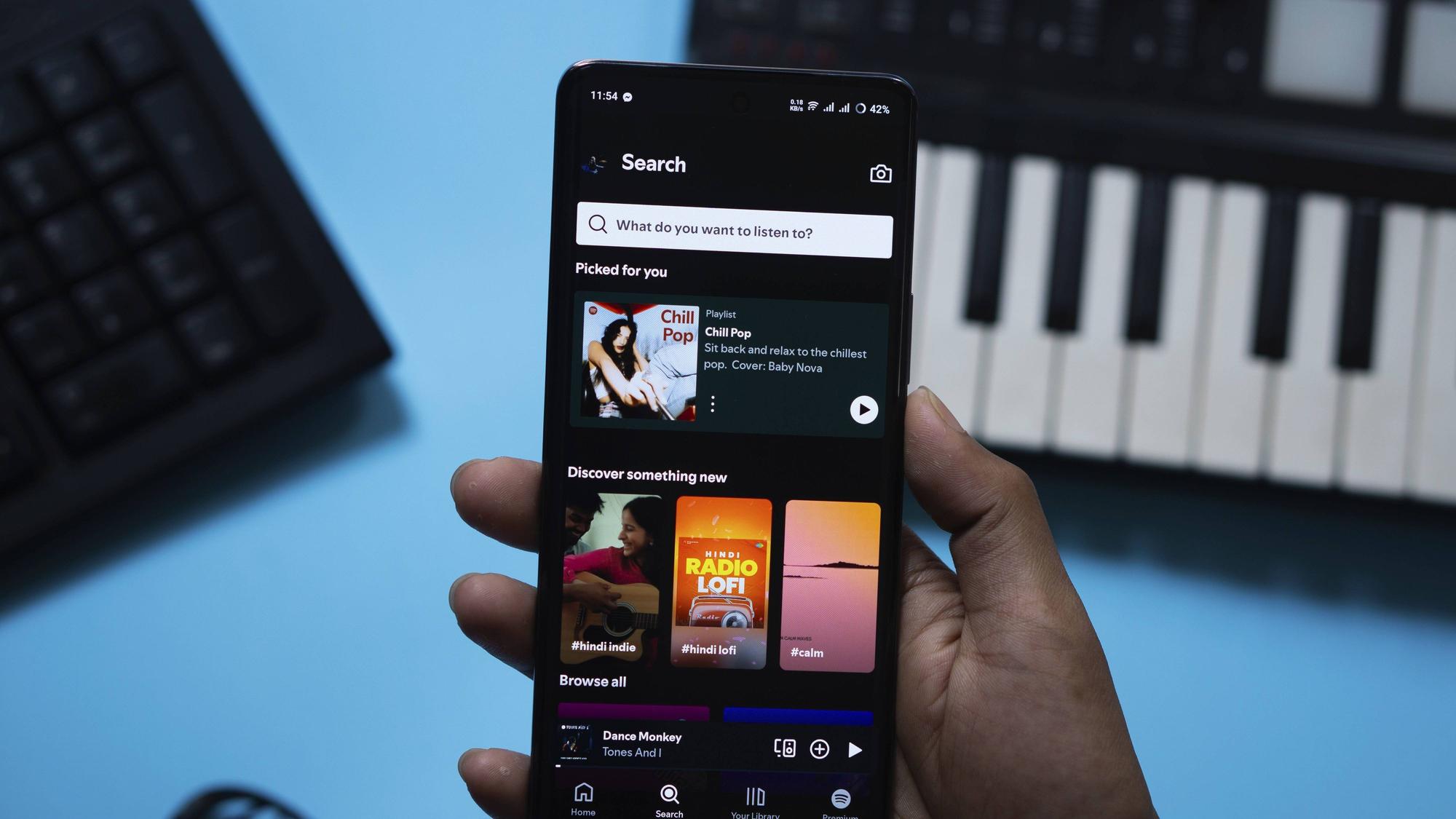 Das Bild zeigt die geöffnete App Spotify auf einem Smartphone, ein Keyboard und eine PC-Tastatur im Hintergrund. Foto: IMAGO/imagebroker