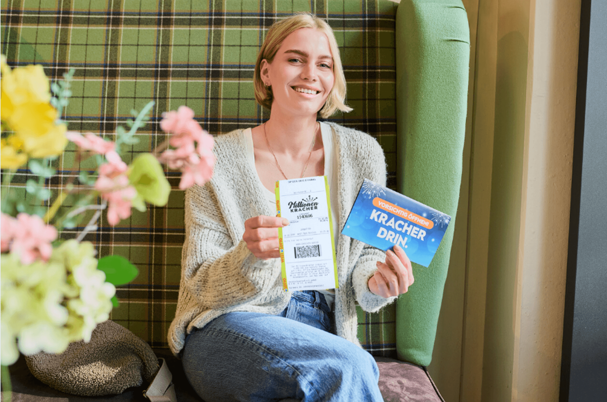 Eine Frau sitzt glücklich auf einem Sofa und hält ein MillionenKracher-Los in der Hand.