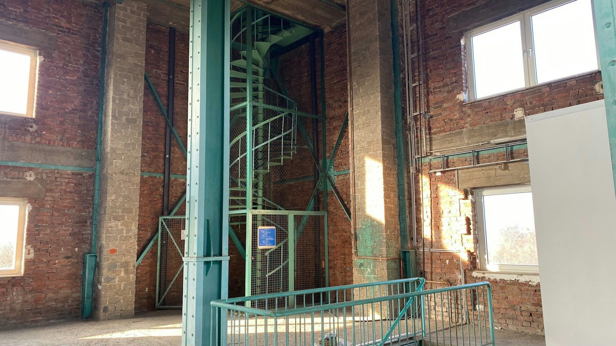 Zu sehen ist ein Raum mit Stahlstützen und dahinter einer Wendeltreppe.