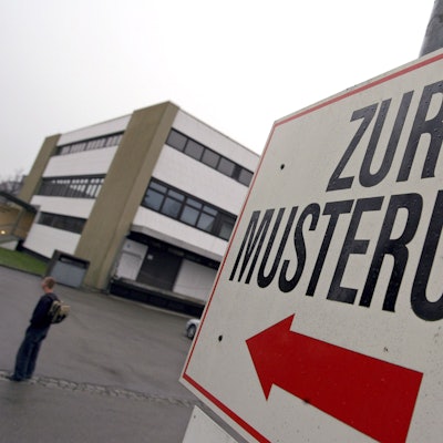 Ein Wehrpflichtiger steht unter einem Hinweisschild mit der Aufschrift «Zur Musterung» vor einem Kreiswehrersatzamt.