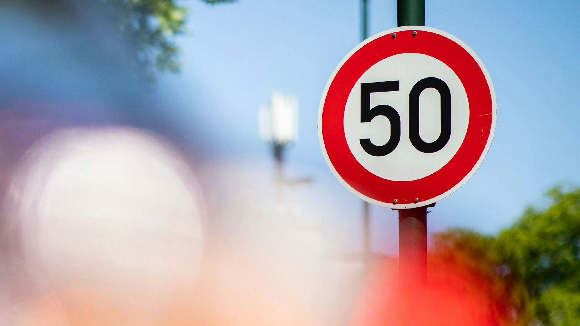 Ein Verkehrsschild zur Geschwindigkeitsbegrenzung auf Tempo 50 steht auf einer Hauptstraße vor geparkten Autos.