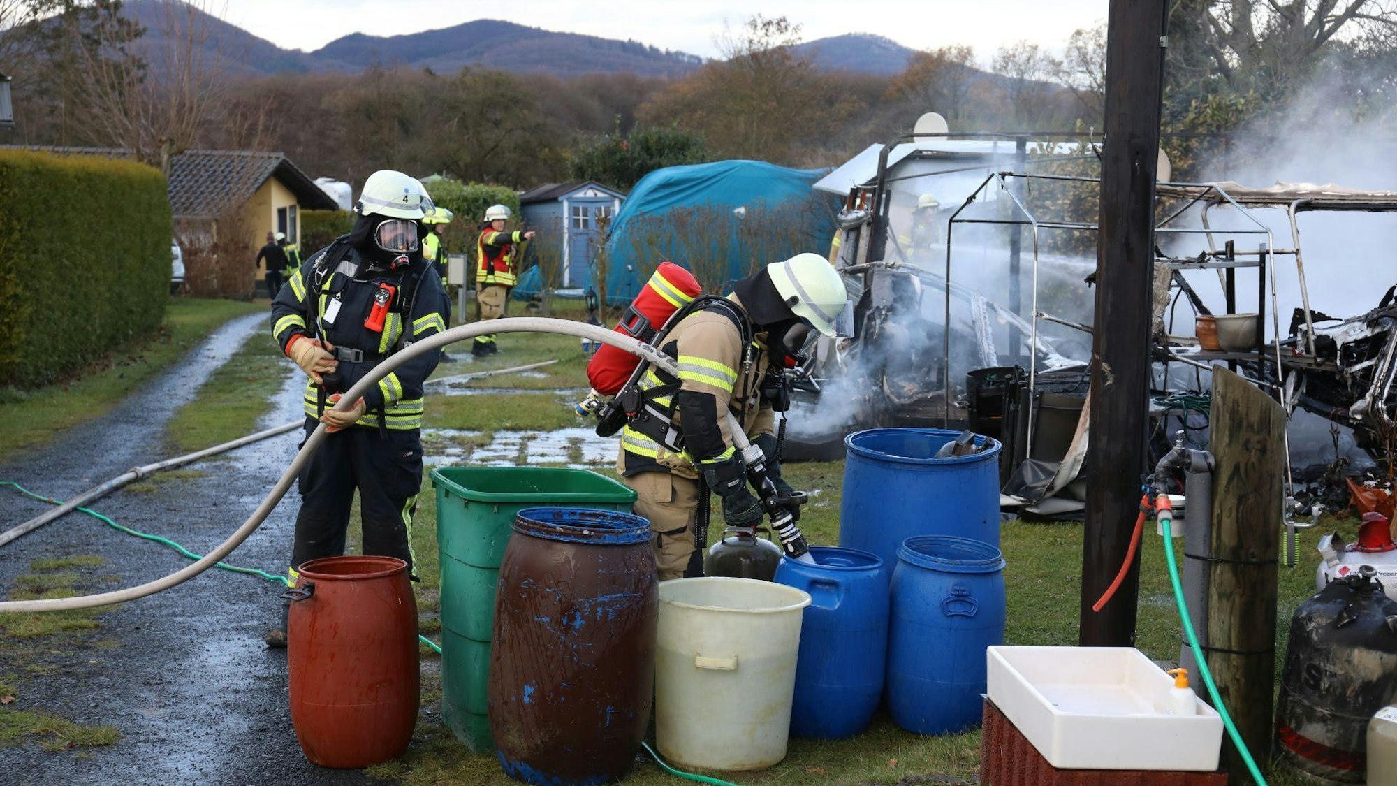 Ein Feuerwehrmann füllt mit einem Löschschlauch große Fässer mit Wasser.